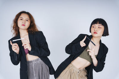 Portrait of lesbian couple holding pen standing against gray background