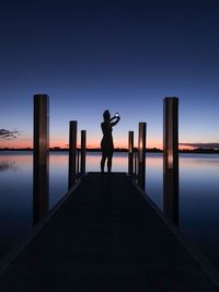 Rear view of silhouette woman standing on pier over sea against sky