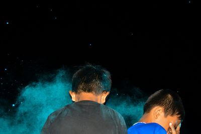 Rear view of boys on illuminated water at night