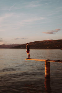 Rear view of woman walking at beach against sky during sunset