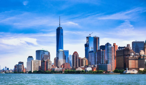 City buildings at waterfront against cloudy sky