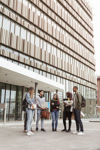 Multi-ethnic students talking while standing against building in university campus