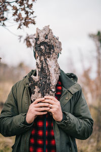 Man covering face with wood while standing in forest