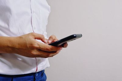 Midsection of man using mobile phone against gray background