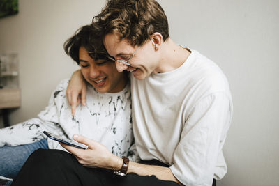 Smiling multi-ethnic male friends sharing smart phone at home