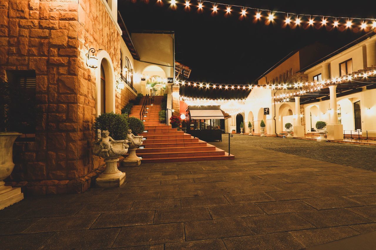 EMPTY FOOTPATH AMIDST ILLUMINATED BUILDINGS