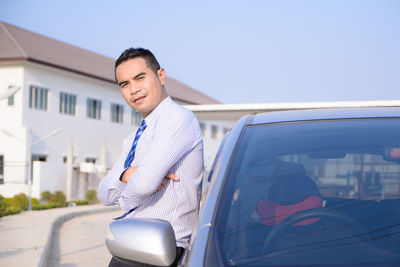 Portrait of businessman standing by car against clear sky