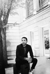 Portrait of young man sitting against building