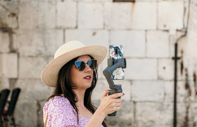 Front view of young woman using gimbal and mobile phone for vlogging on her travels.