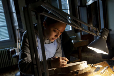 Female craftsman violin maker working on a new violin in the workshop