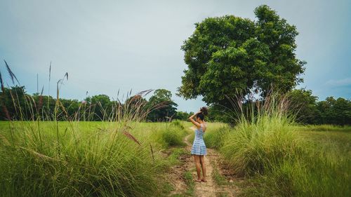 Rear view of girl walking on field against sky