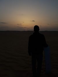 Rear view of silhouette man standing on beach against sky during sunset