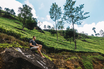 Man sitting on field against trees