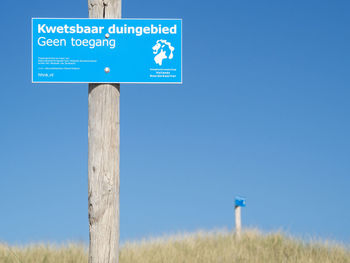 Low angle view of road sign against clear blue sky