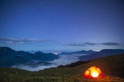 Tent on field against mountain range at night