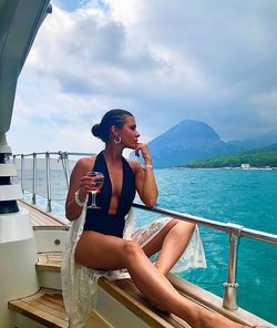 Thoughtful woman wearing swimwear while having wine on boat in sea against cloudy sky