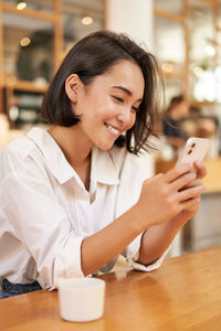 Young woman using mobile phone at table