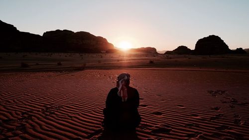 Woman standing on sand against clear sky during sunset