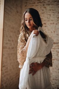 Woman holding wedding dress while standing against wall