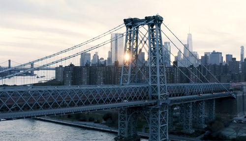 Suspension bridge in city against cloudy sky