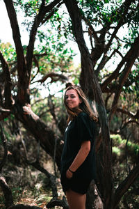 Portrait of young woman standing by tree in forest