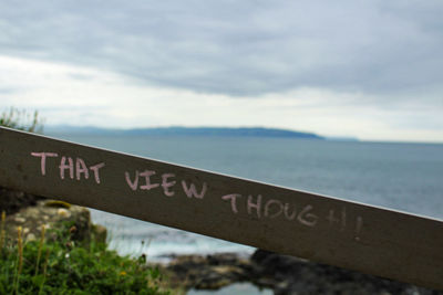 Close-up of information sign by sea against sky