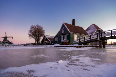 Snow covered houses by building against clear sky during winter