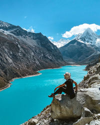 Portrait of woman sitting on rock by mountains against blue sky
