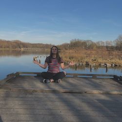 Woman sitting by lake against sky