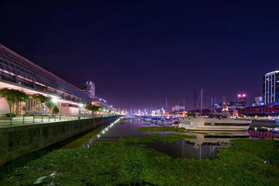 Boats moored on river amidst buildings against sky at night