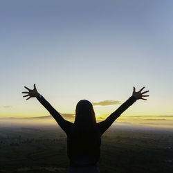 Silhouette woman with arms raised against sky during sunset
