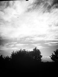 Low angle view of trees against cloudy sky