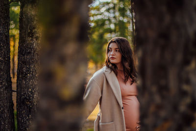 Beautiful woman standing by tree trunk in forest