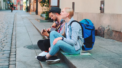 Man using mobile phone while sitting on footpath