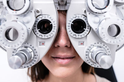 Smiling female patient in modern phoropter checking vision during visit in modern ophthalmological clinic