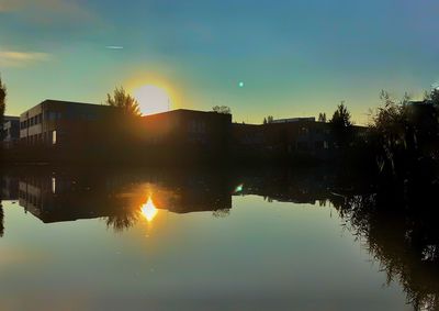 Silhouette buildings by lake against sky during sunset