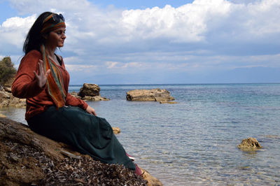 Rear view of woman sitting on rocks by sea