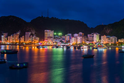 Illuminated city by sea against sky at night