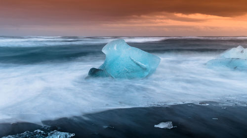 Ice floating on sea against sky during sunset