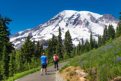 Rear view of people walking on mountain against blue sky