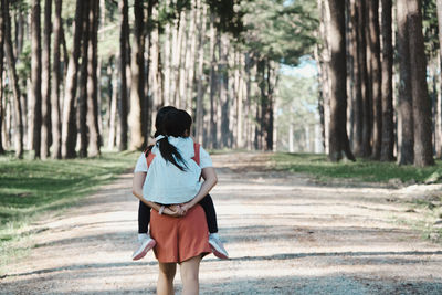 Rear view of mother piggybacking daughter at park