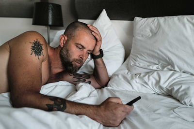 Tattooed man laying in bed using phone