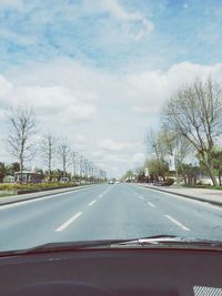 Road amidst trees against cloudy sky seen through car windshield