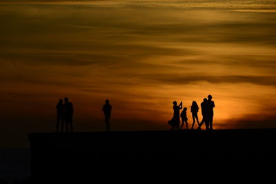 Silhouette people standing on beach against sky during sunset