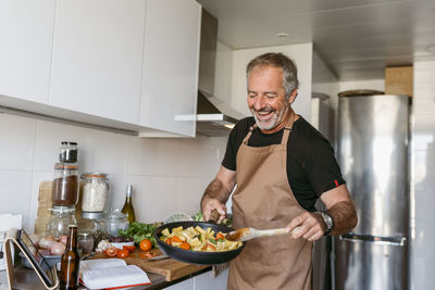 Smiling mature man preparing pasta while standing in kitchen at home