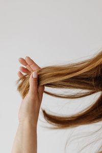 Midsection of woman holding hair against white background
