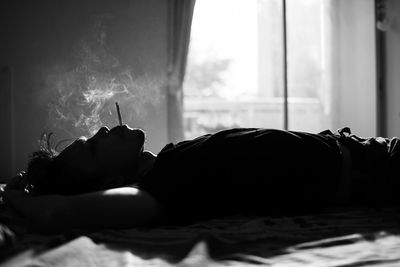 Side view of man smoking cigarette while lying on bed at home