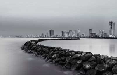 Rock jetty reaching into the sea with city in the background