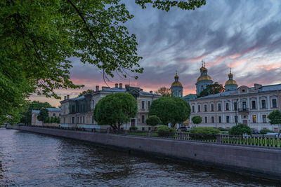 View of buildings by river against cloudy sky