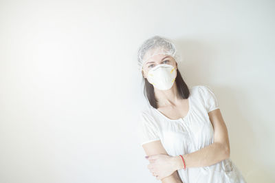 Portrait of woman wearing mask standing against white background